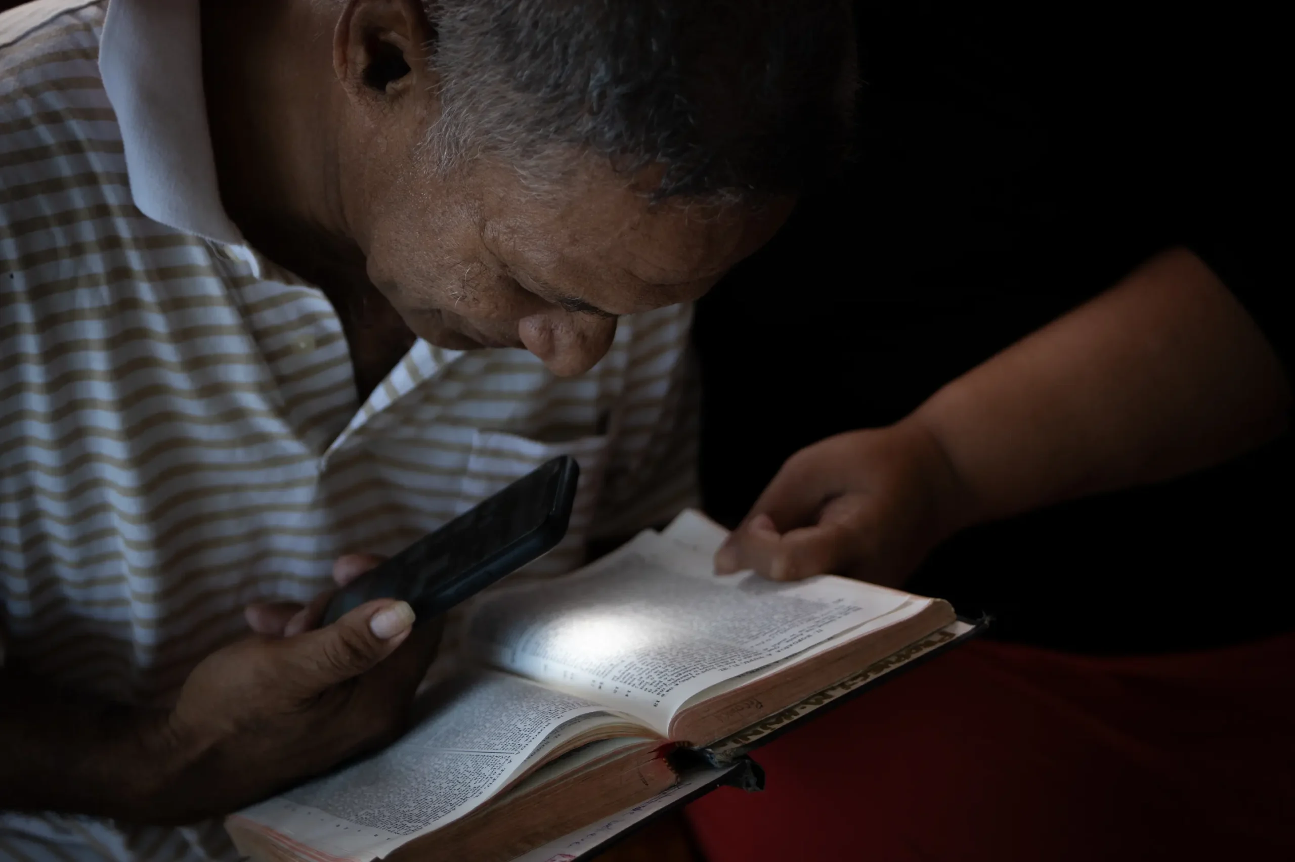 Pateki using a phone light to try and read the bible