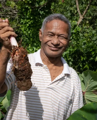 Pateki smiling and holding a taro freshly pulled from his garden